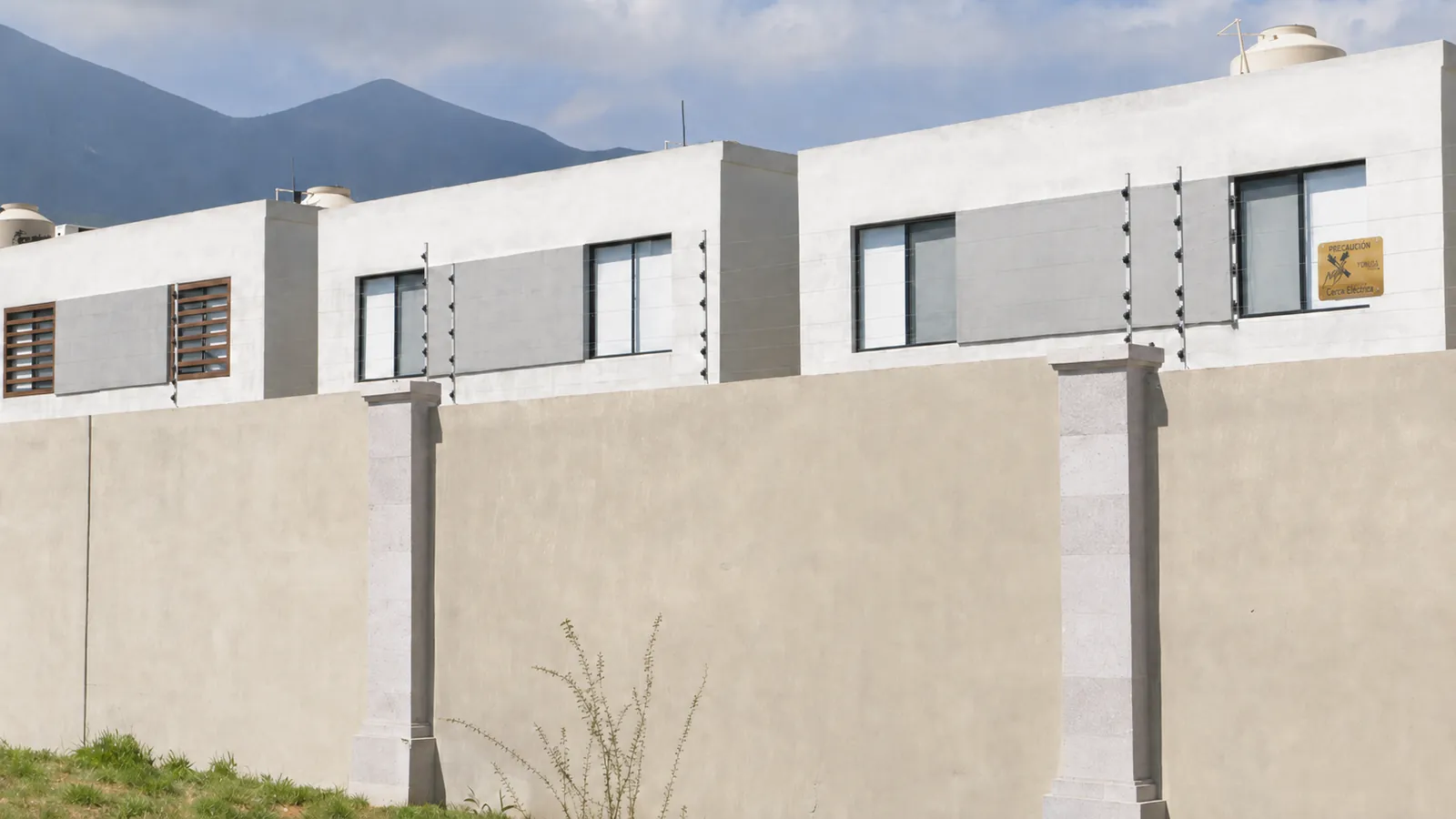 Detalle del montaje: aisladores negros y seis hilos de acero tensados sobre el pretil de una casa, con la sierra de Monterrey al fondo